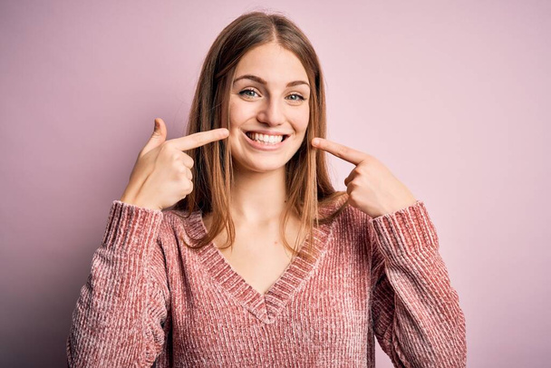 Young beautiful redhead woman wearing casual sweater over isolated pink background smiling cheerful showing and pointing with fingers teeth and mouth. Dental health concept. - Fotó, kép