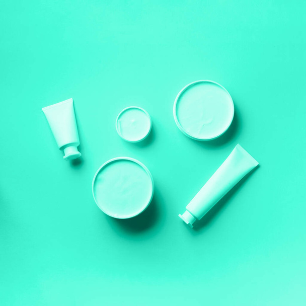 Cosmetics, skin care, beauty, body treatment concept. White cosmetic jar, tube, bottle and tropical monstera leaf over mint color background. Trendy green and turquoise color. - Photo, Image