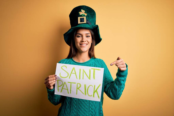 Egy nő zöld kalapban ünnepli a Szent Patrik napot, zászlót tart szent Patrick üzenetével, nagyon boldog, hogy mutogathat kézzel és ujjal. - Fotó, kép