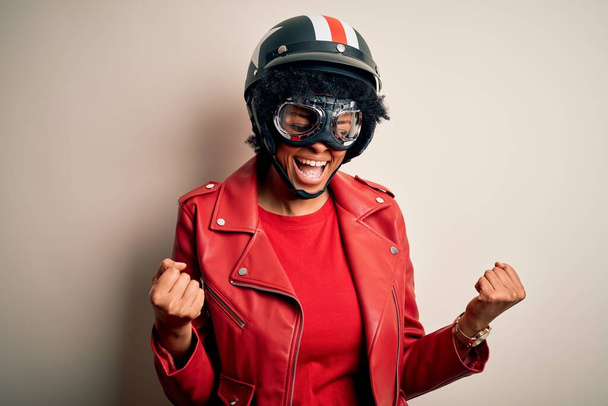 Young African American afro motorcyclist woman with curly hair wearing motorcycle helmet very happy and excited doing winner gesture with arms raised, smiling and screaming for success. Celebration concept. - Foto, immagini