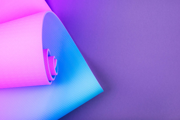 Top view of neon colored blue pink yoga mat on violet background. Space for text. - Foto, afbeelding