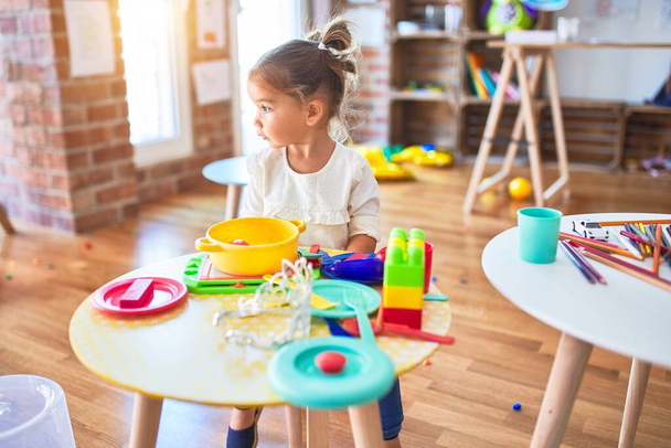Молодой красивый ребенок играет со столовыми приборами и пищевыми игрушками на столе в детском саду
 - Фото, изображение