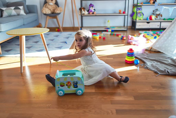 Imádnivaló szőke kisbaba játszik autós játék körül sok játék óvodában - Fotó, kép
