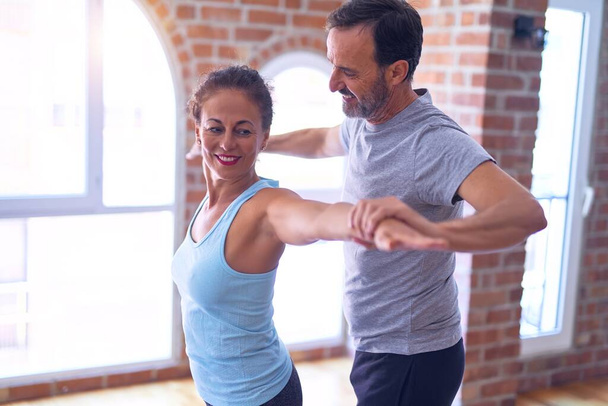 Middle age beautiful sporty couple smiling happy. Standing doing stretching after class ofyoga at gym - 写真・画像