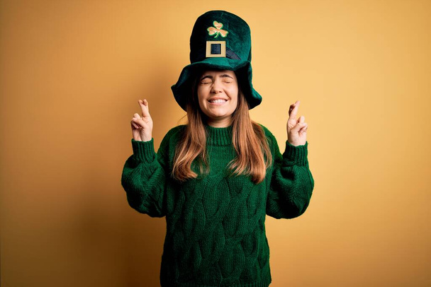 Mladá krásná bruneta žena v zeleném klobouku na svatém Patrickovi den oslav gestikuluje prstem přes rameno s nadějí a zavřenýma očima. Štěstí a pověrčivý koncept. - Fotografie, Obrázek