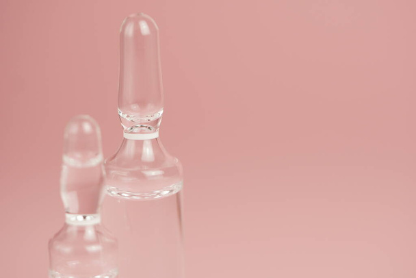 Ampollas médicas de vidrio sobre fondo rosa de cerca, espacio para copiar, enfoque selectivo
. - Foto, imagen