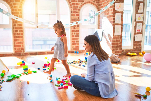 Beyaz kız çocuk, bayan öğretmenle oyun oynayıp öğreniyor. Anne ve kız oyun odasında oyuncaklarla oynuyorlar. - Fotoğraf, Görsel