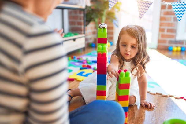 Mooie leraar vrouw en peuter spelen met bouwstenen rond veel speelgoed op de kleuterschool - Foto, afbeelding