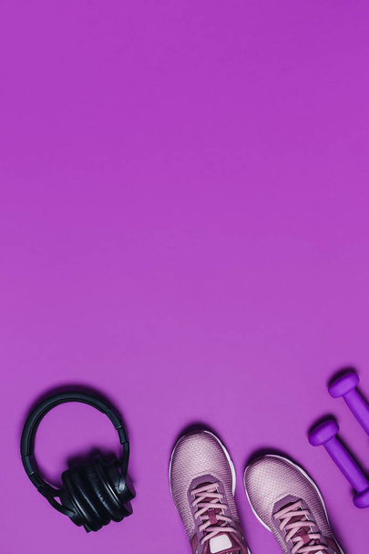 Sport lapos fekvésű, tornacipővel, súlyzóval és fejhallgatóval lila háttérrel. Függőleges kép. - Fotó, kép