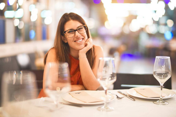 Young beautiful girl smiling happy and confident sitting on chair at restaurant. Relaxing with a smile on face - Foto, Imagen