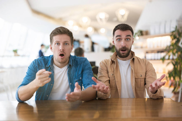 two bewildered men looking shocked while sitting in the cafe during lunch break, mood and emotions concept. - Foto, imagen