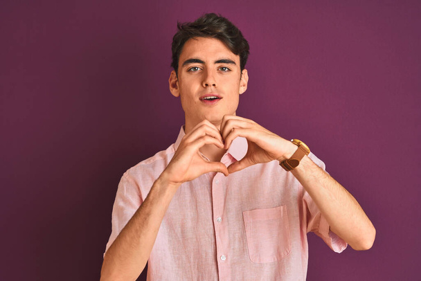 Teenager boy wearing pink shirt standing over purple isolated background smiling in love showing heart symbol and shape with hands. Romantic concept. - Photo, Image