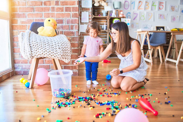 Молодий красивий вчитель і малюк грають з будівельними блоками іграшки в дитячому саду
 - Фото, зображення