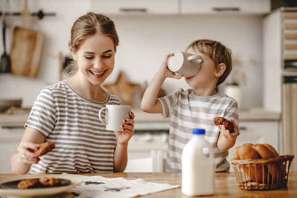 家族の朝食の準備だ母親と子供の息子はパンを切ってモーニンで牛乳とクッキーを食べる - 写真・画像
