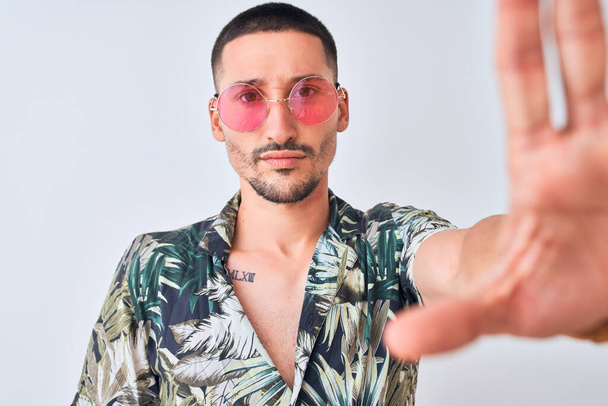 Young handsome man wearing Hawaiian sumer shirt and pink sunglasses over isolated background with open hand doing stop sign with serious and confident expression, defense gesture - Zdjęcie, obraz