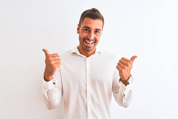 Молодой привлекательный бизнесмен в элегантной рубашке на изолированном фоне знак успеха делает позитивный жест с рукой, большие пальцы вверх улыбается и счастлив. Веселое выражение лица и жест победителя
. - Фото, изображение