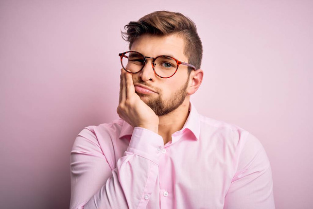 Young handsome blond man with beard and blue eyes wearing pink shirt and glasses thinking looking tired and bored with depression problems with crossed arms. - Photo, Image