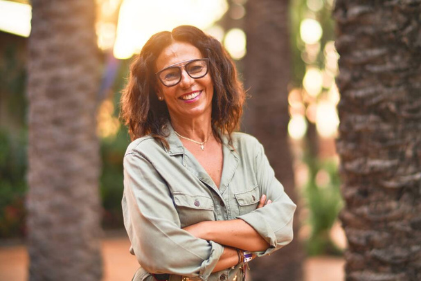 Schöne Frau mittleren Alters, die eine Brille trägt und glücklich und zuversichtlich lächelt. Mit einem Lächeln im Stadtpark stehen - Foto, Bild