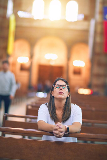 Young beautiful woman praying on her knees in a bench at church - Foto, Imagem