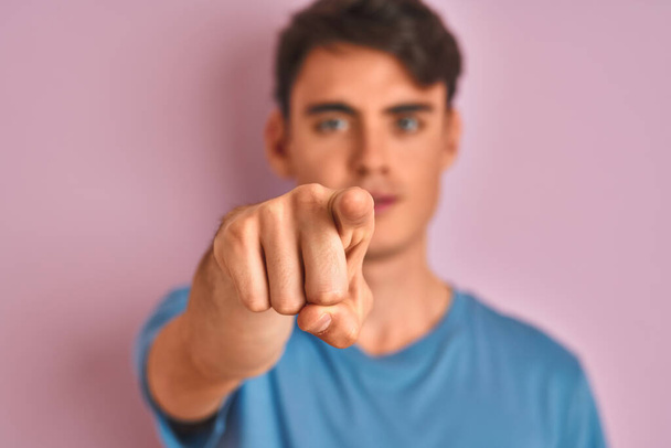 Мальчик-подросток в обычной футболке стоит на синем изолированном фоне, указывая пальцем на камеру и на тебя, знак руки, позитивный и уверенный жест спереди
 - Фото, изображение