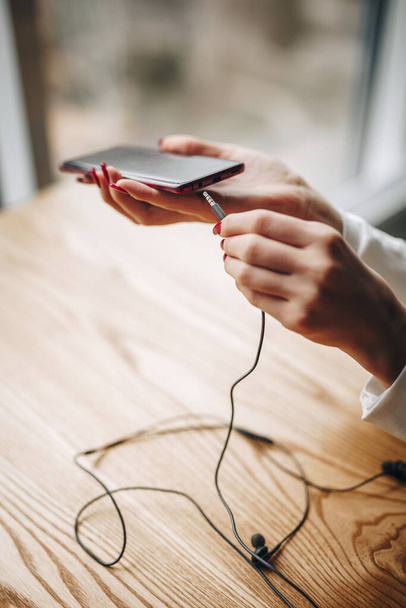 girl puts black wired headphones into the phone - Фото, изображение