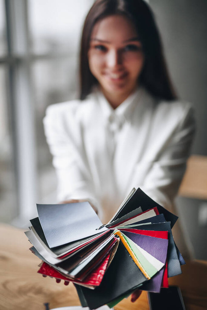 meisje in het kantoor toont een verzameling van gekleurde stukken stof - Foto, afbeelding