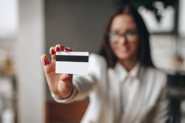 girl shows a credit card in her right hand, with a blurred background - Φωτογραφία, εικόνα
