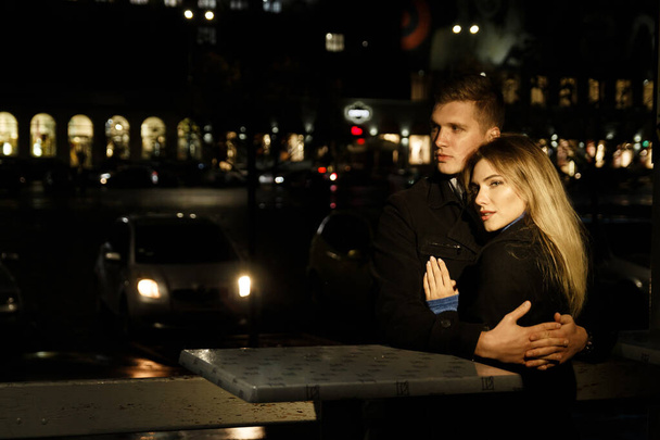 couple in love embracing against a dark background, night, rain, buildings in the city, a park, smiling,attraction. the guy hugs the girl. Valentine's Day dark street and rain - Foto, afbeelding
