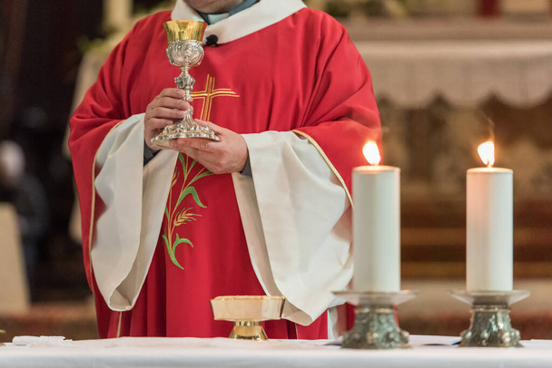 Ministro mostrando el cáliz sagrado durante el rito de la Santa Cena en la misa católica
 - Foto, imagen
