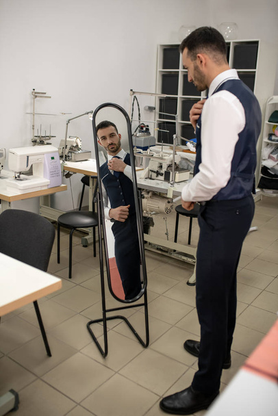 Male tailor looking in the mirror, fixing tie - Fotó, kép