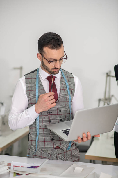 Male tailor holding laptop in one hand and pencil in another - Foto, Imagen