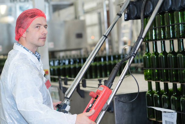 worker operating controls in wine bottling plant - Foto, afbeelding