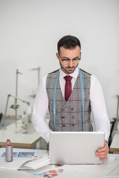 Male fashion designer standing, checking something on laptop - Foto, Imagen
