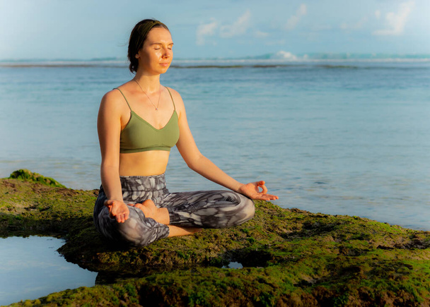 Genç beyaz kadın, meditasyon yapıyor, yoga yapıyor ve plajda pranayama yapıyor. Günbatımı yoga antrenmanı. Eller Gyan Mudra 'da. Lotus pozu. Kapalı gözler, rahatla, konsantre ol. Melasti plajı, Bali, Endonezya - Fotoğraf, Görsel