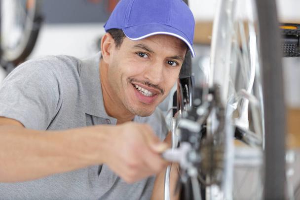 handsome man in uniform working with bicycles wheel - Foto, afbeelding