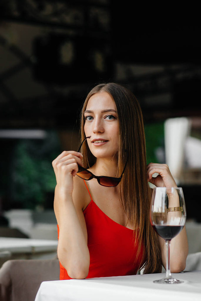 Beautiful young girl sits and drinks wine on the veranda of a beautiful house. Holiday. - Foto, imagen