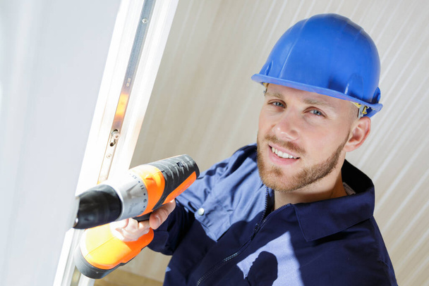 male builder using a drill to install a window - Foto, afbeelding