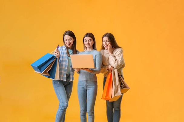Young women with laptop and shopping bags on color background - Foto, Imagen