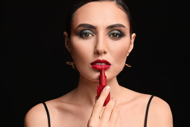 Beautiful young woman applying makeup against dark background - Photo, Image