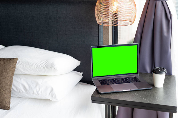 Coffee Cup To Go and a Laptop on the bedside. Technology and home concept. Green template on screen - Photo, Image