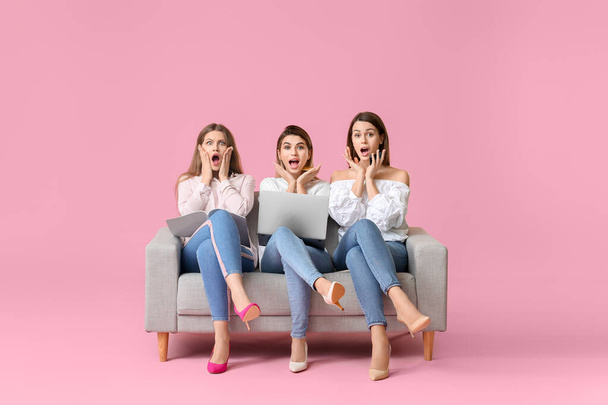 Surprised young women with laptop sitting on sofa against color background. Online shopping concept - Photo, Image