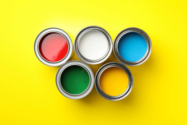 Cans of different paints on yellow background, top view - Фото, изображение