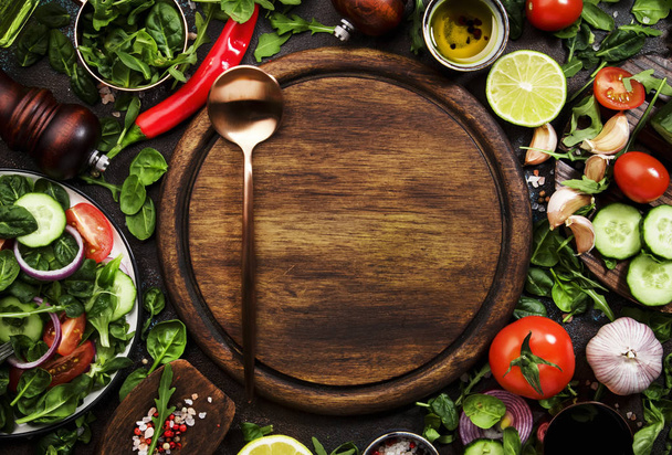 Sağlıklı vejetaryen malzemeleri. Yeşil otlar, domatesler, salatalıklar, baharatlar ve kahverengi mutfak masasında ahşap tahtalı yağ. Üst görünüm, boşluğu kopyala. Vejetaryen, çiğ, temiz yeme konsepti - Fotoğraf, Görsel