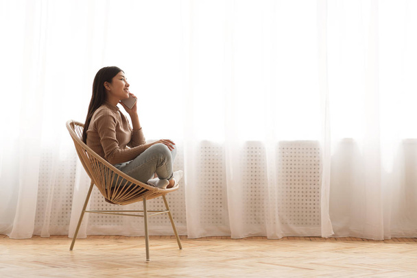 Enjoying home comfort. Girl talking on phone in cozy chair - Фото, зображення