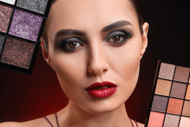 schöne junge Frau mit Kosmetik vor dunklem Hintergrund - Foto, Bild