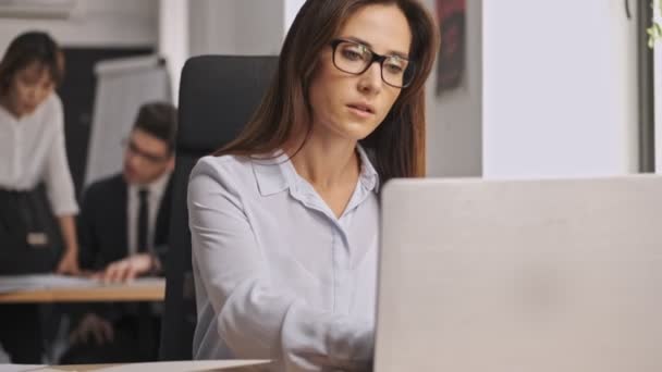 Serious businesswoman wearing eyeglasses working with documents and laptop computer while sitting in office - Filmagem, Vídeo