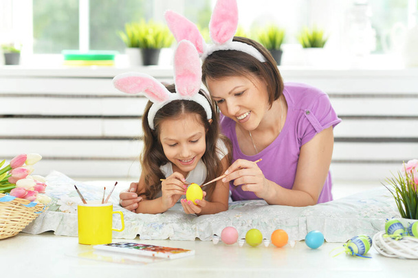  Mother with daughter wearing rabbit ears decorating  Easter eggs at home  - Foto, Imagem