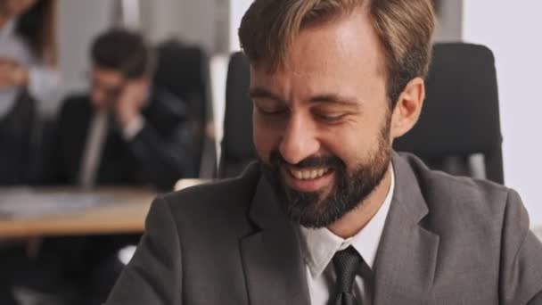 Close up view of Cheerful businessman in formal suit using looking away and down while sitting by the table in office - Séquence, vidéo