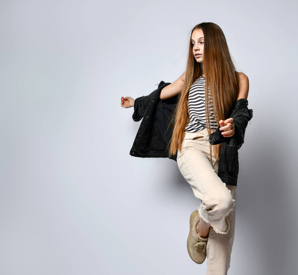 Adolescent in striped t-shirt, black denim jacket, pants and sneakers. She is posing isolated on white background. Close up - Photo, image