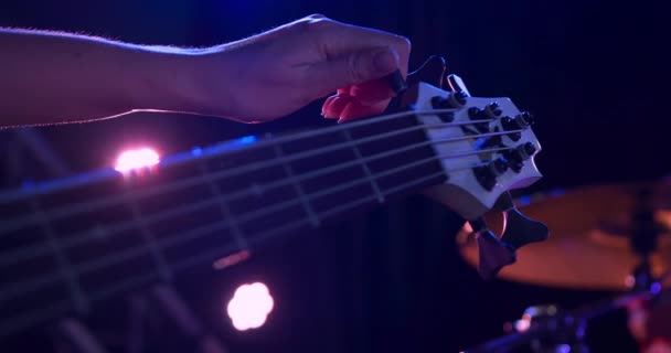 Close up detail of a mixed race female bass player rehearsing at a music venue before a performance, sitting and tuning her acoustic guitar in slow motion - Metraje, vídeo